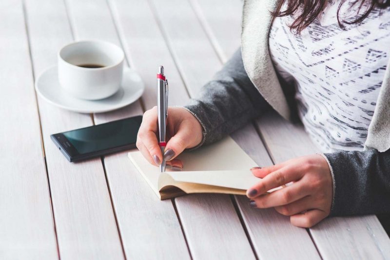 woman writing 4 fun with a pen and drinking coffee