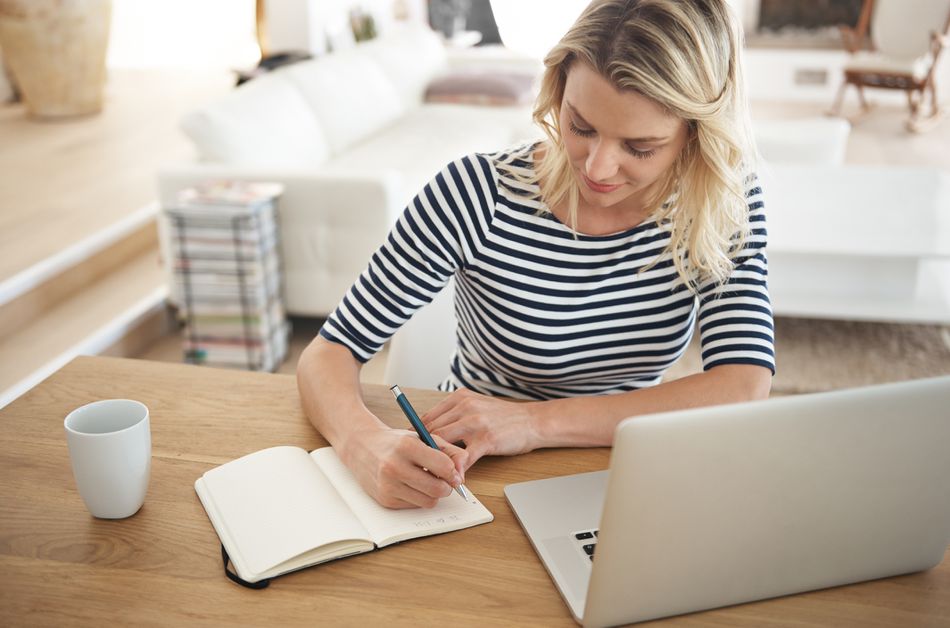 woman writing in notebook by a laptop